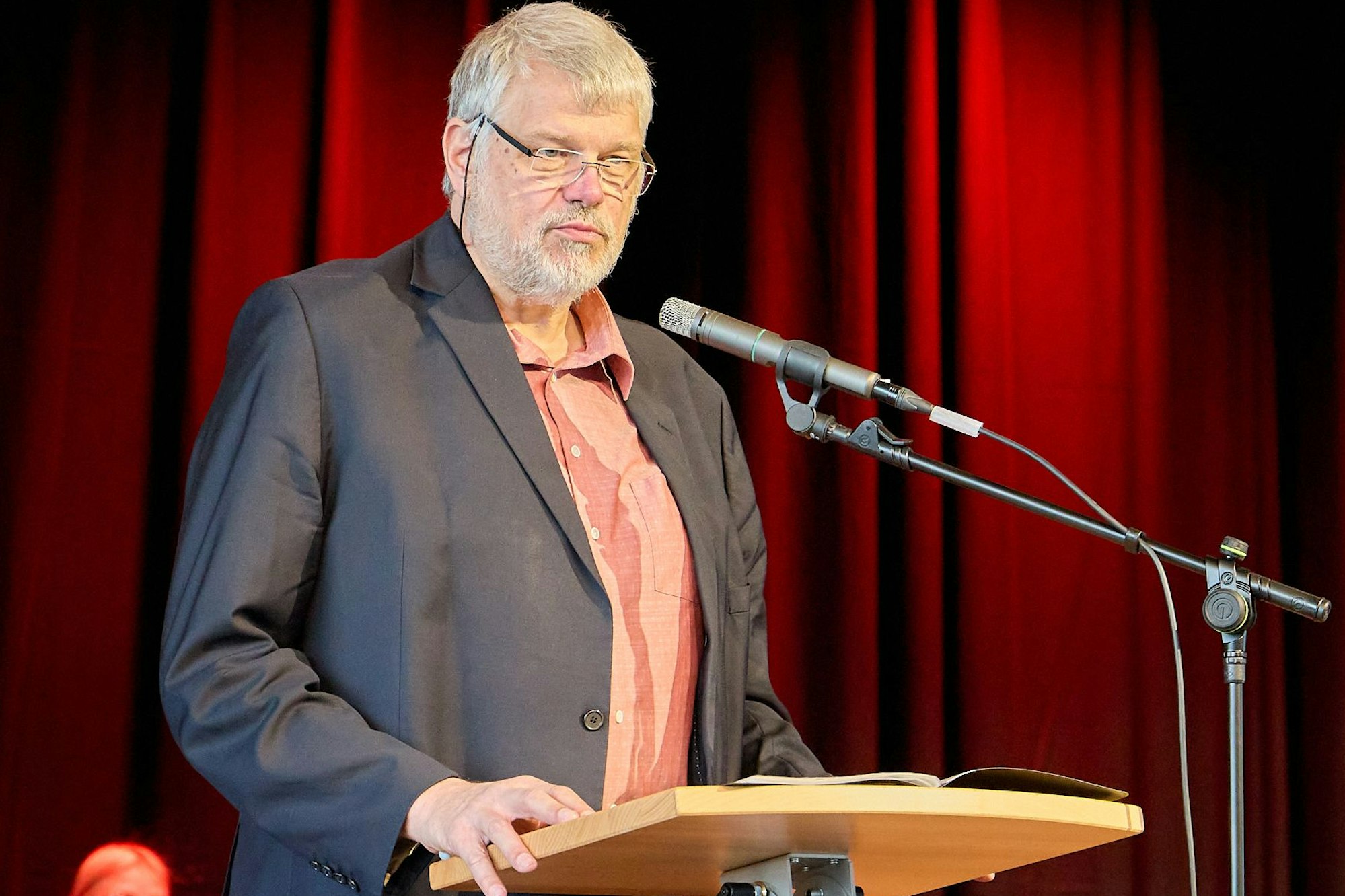 Georg Jöbkes steht vor einem roten Vorhang an einem Rednerpult.
