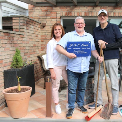 Zwei Männer und zwei Frauen lächeln in die Kamera, einer hält ein Firmenschild im Arm.