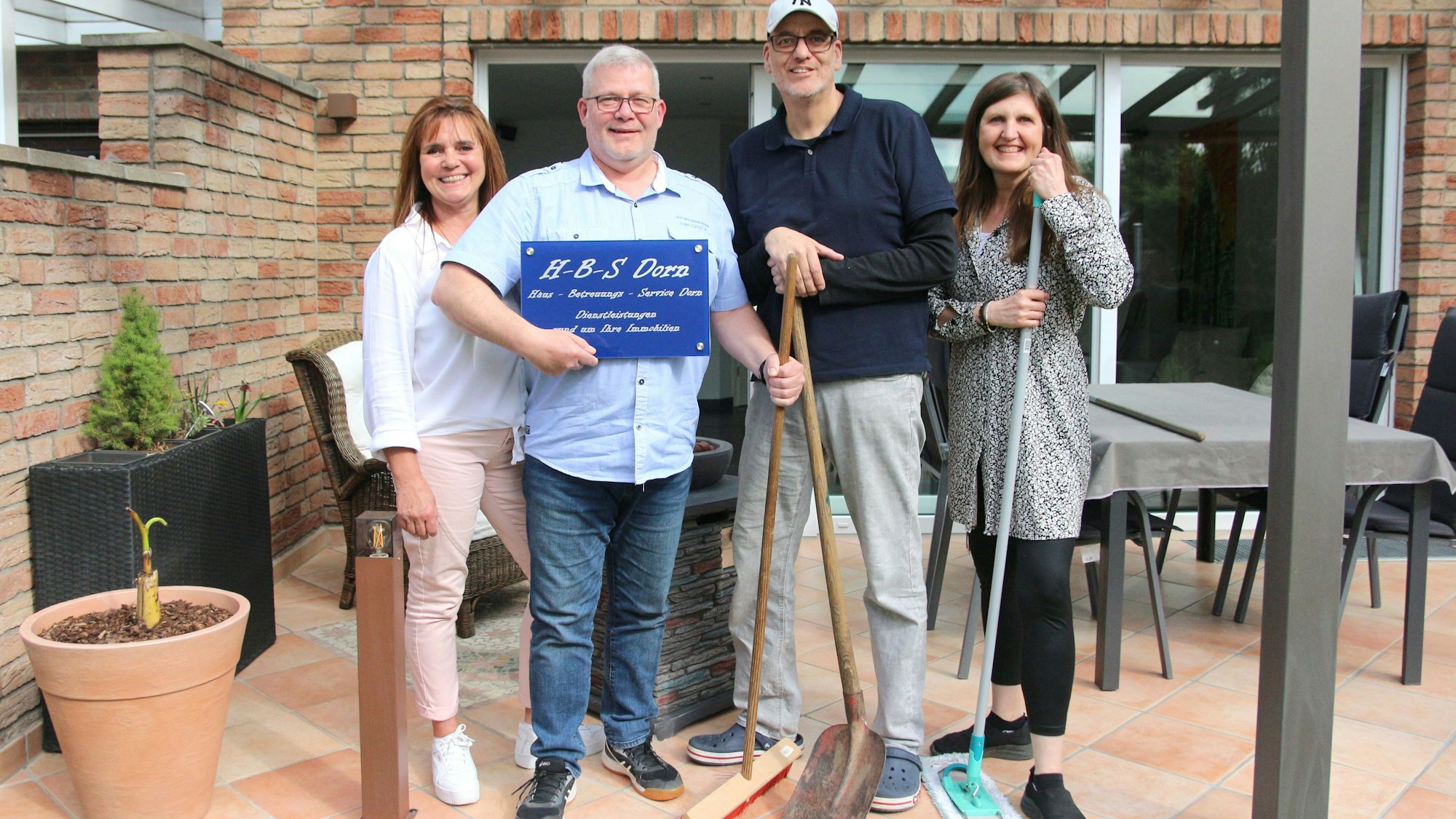 Zwei Männer und zwei Frauen lächeln in die Kamera, einer hält ein Firmenschild im Arm.