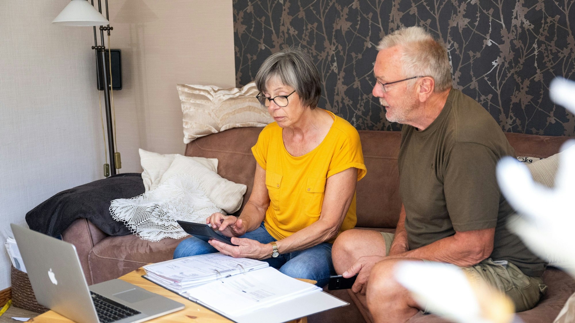 2 Menschen sitzen vor einem Rechner und einem Ordner.