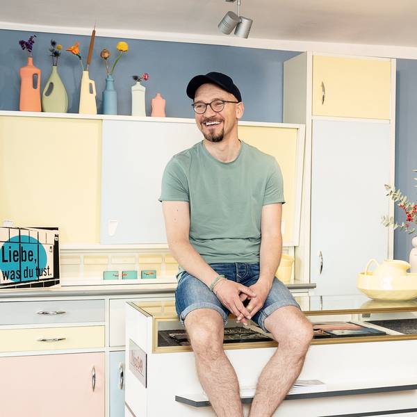 Ein Mann mit blauer Kappe, Brille und Bart sitzt auf einem Küchenbüfett.