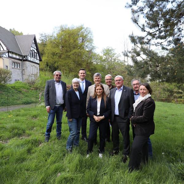 Eine Gruppe von Männern und Frauen auf einer Wiese, im Hintergrund ein Forsthaus.