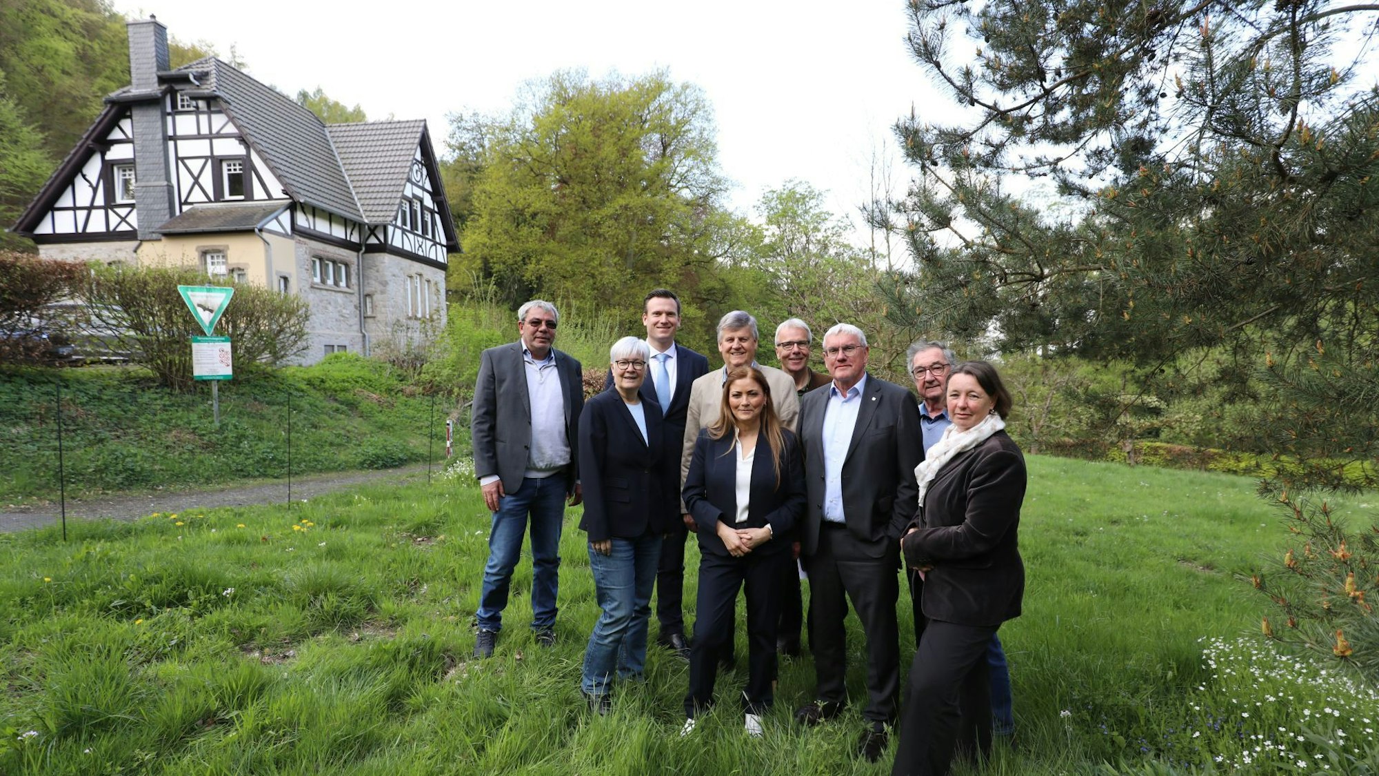 Eine Gruppe von Männern und Frauen auf einer Wiese, im Hintergrund ein Forsthaus.