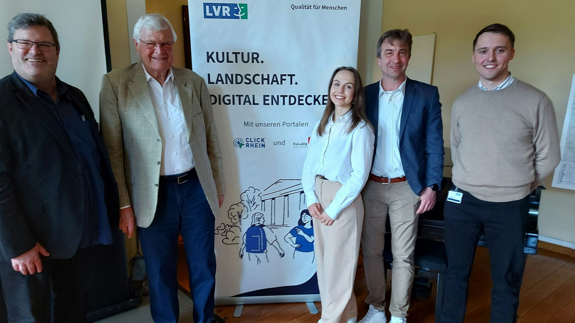 Vier Männer und eine Frau stehen vor einem Plakat des Landschaftsverbands Rheinland.