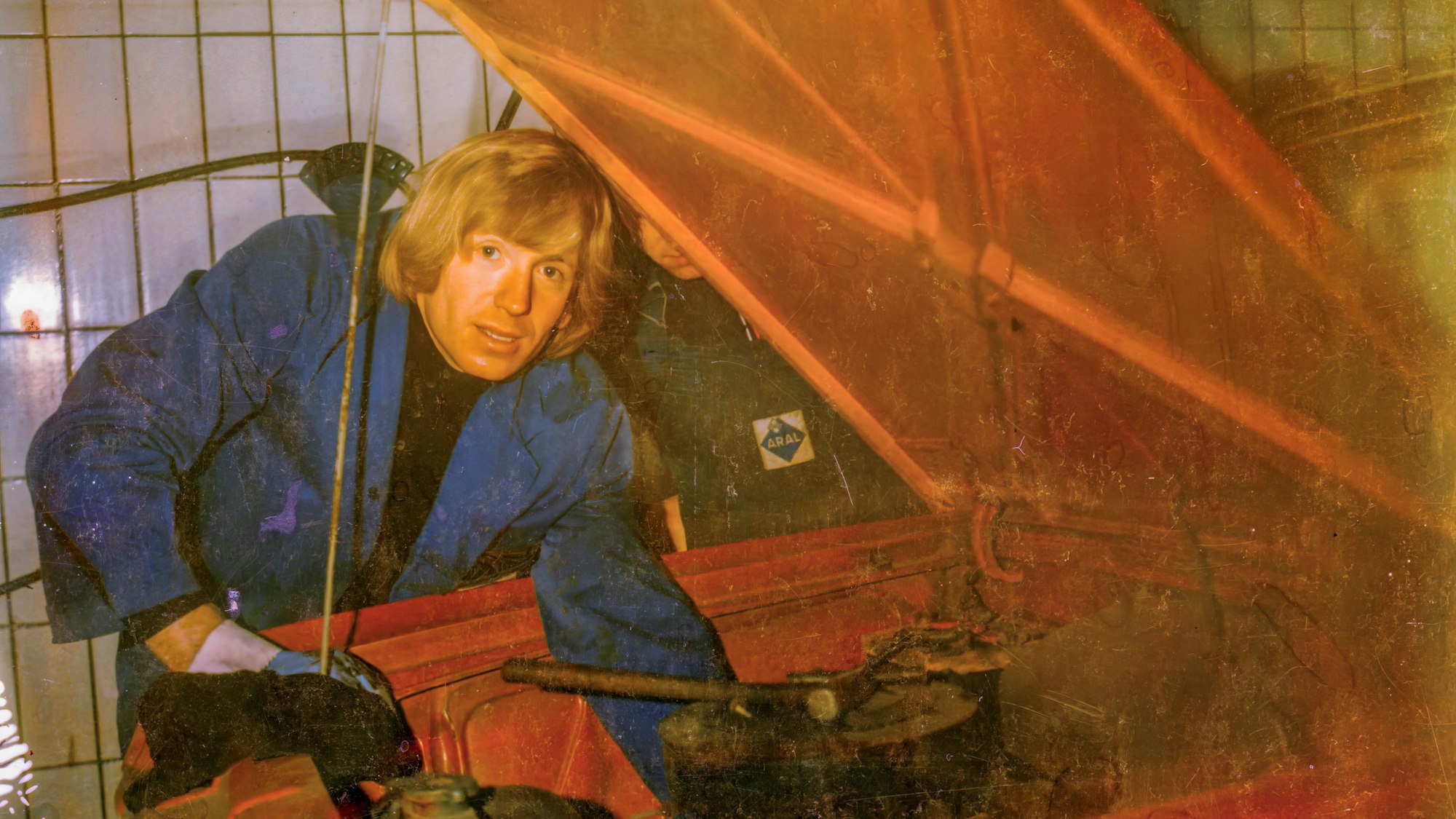 Ein Mann ist über die offene Motorhaube eines Autos gebeugt.