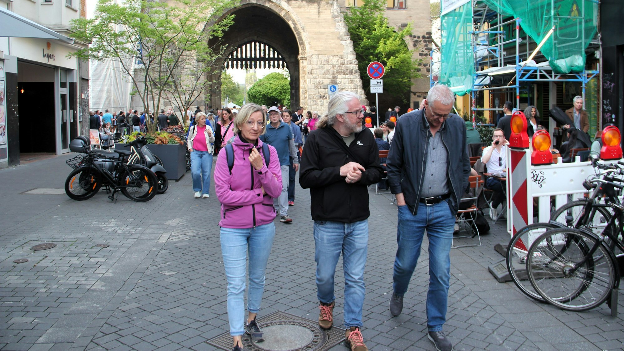 Drei Menschen laufen über den Eigelstein, im Hintergrund ist die Eigelsteintorburg sehen.