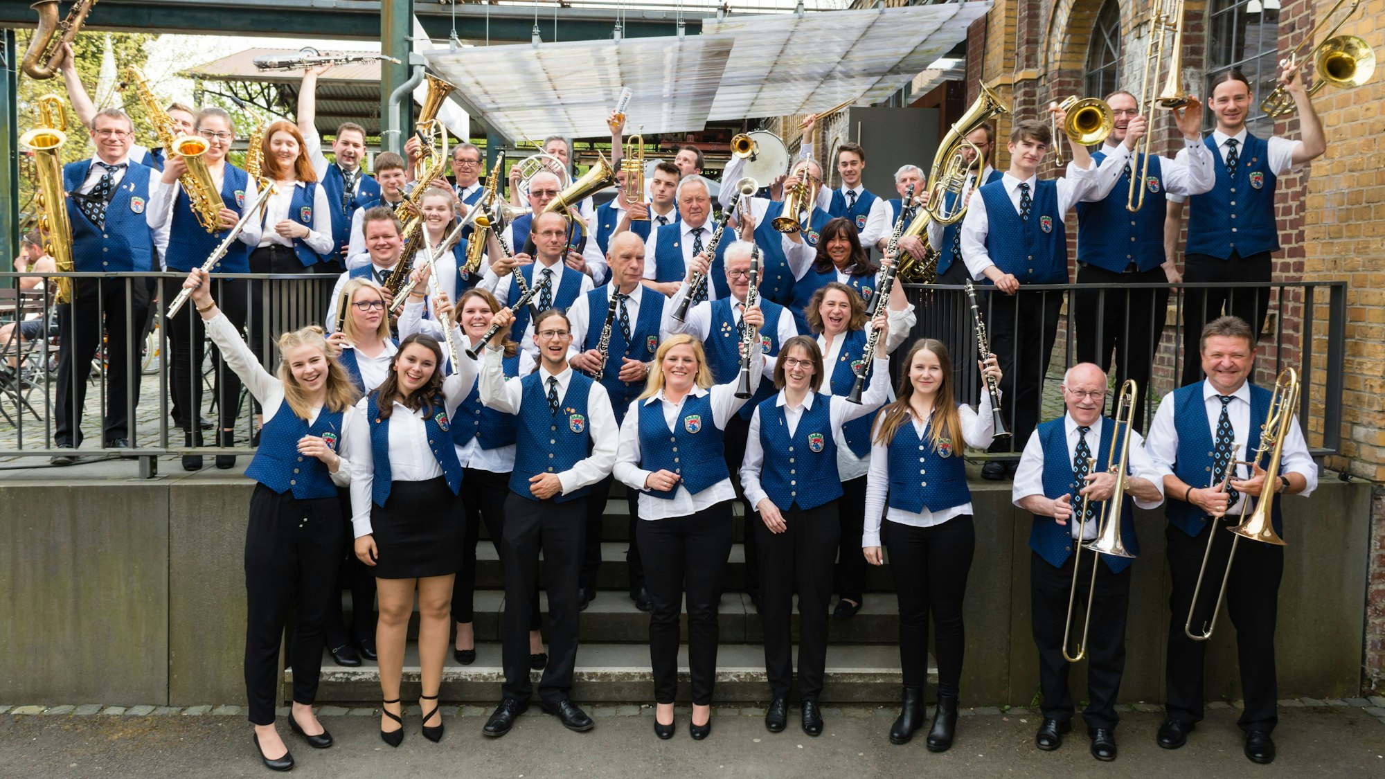 Männer und Frauen des Chors blicken in die Kamera und halten ihre Instrumente in die Höhe.