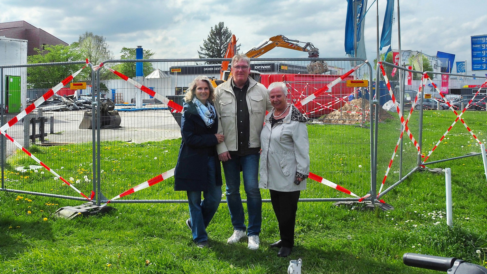 Ein Mann steht mit seiner Frau und seiner Mutter vor dem Bauzaun, hinter der die Aral-Tankstelle in Zollstock abgerissen wird.