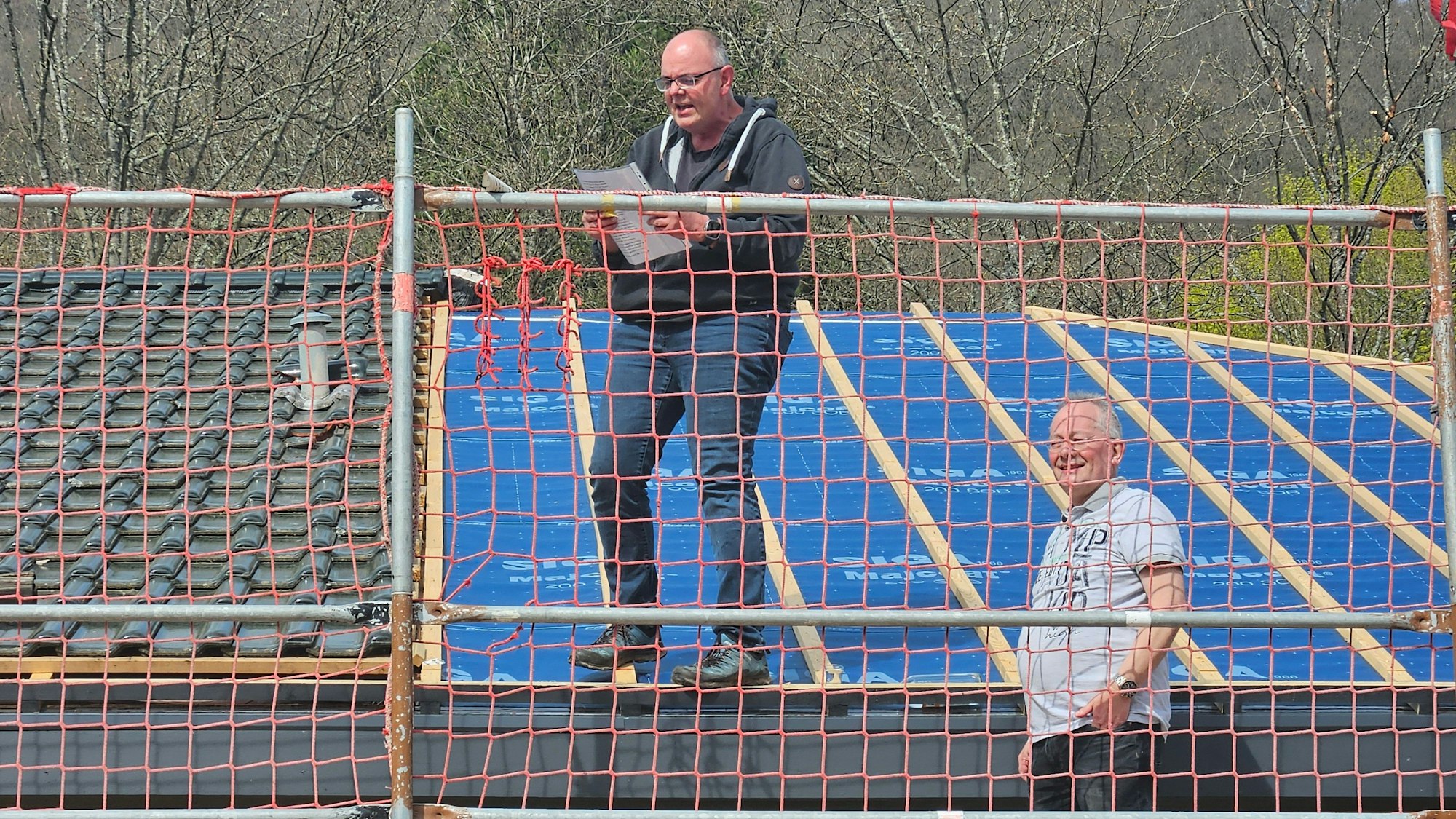 Ein Mann steht auf einem Dachsparren, ein anderer daneben auf einem Gerüst.