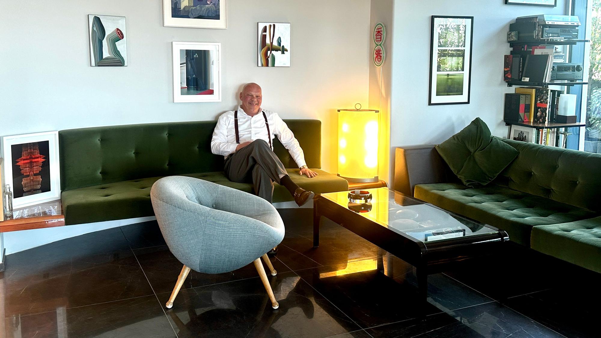 Ein Mann in weißem Hemd und Hosenträgern sitzt auf einem grünen Sofa.