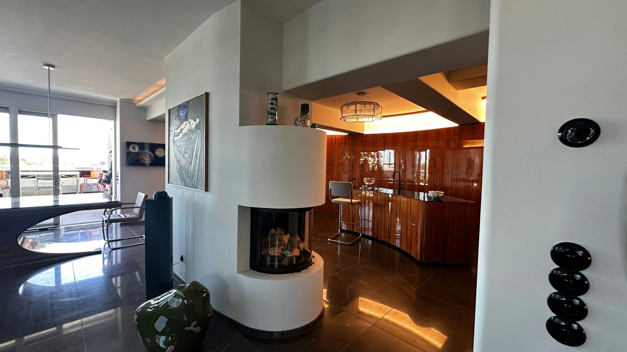 Blick in einen hochwertigen Innenraum, ein halbrunder Kachelofen trennt einen Barbereich vom Essbereich.