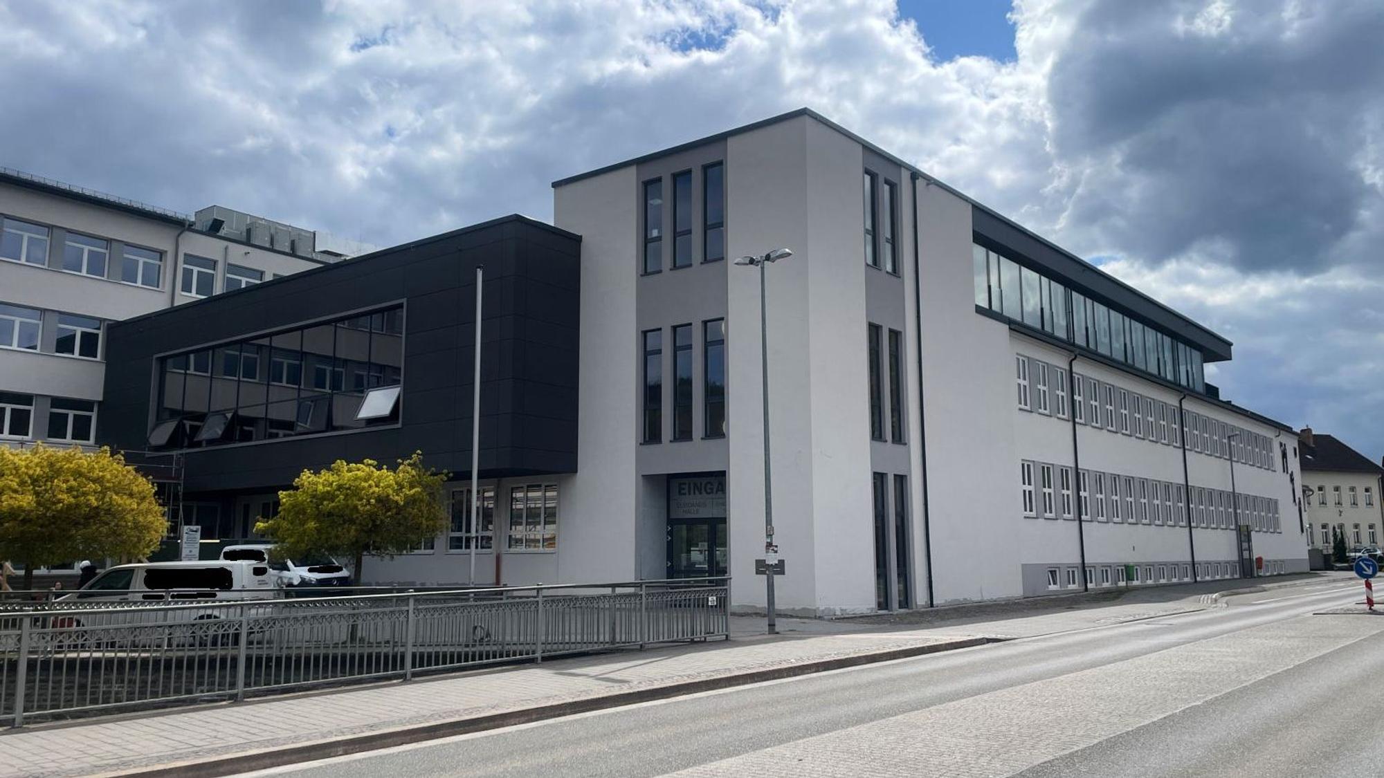 Die dunkle Fassade des neuen Gebäudeteils hebt sich von der hellen Front der Schule ab.