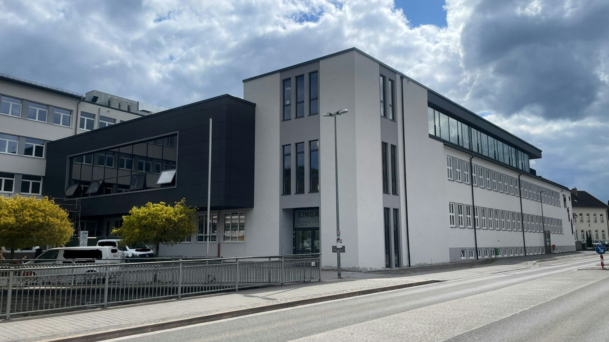 Die dunkle Fassade des neuen Gebäudeteils hebt sich von der hellen Front der Schule ab.