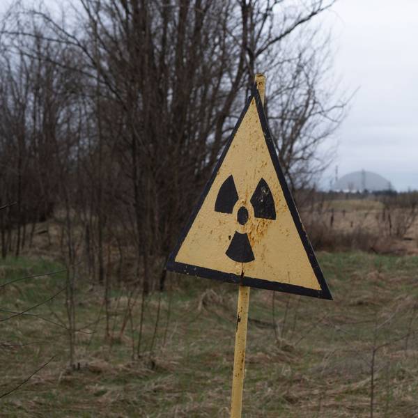 09.04.2026, Ukraine, Tschernobyl: Ein Radioaktivitäts-Warnzeichen, im Hintergrund das Kernkraftwerk Tschernobyl, aufgenommen am 9. April 2026. Was als harmloser Sicherheitstest begann, entwickelte sich am 26. April 1986 zur bedeutendsten Atomkatastrophe der Geschichte. An diesem Tag explodierte Reaktor 4 des Wladimir-Iljitsch-Lenin-Kernkraftwerks, weitläufig bekannt als Kernkraftwerk Tschernobyl. Foto: Nina Mesitz/APA/dpa +++ dpa-Bildfunk +++