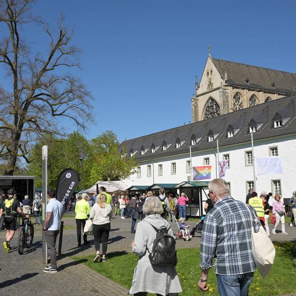 Der Altenberger Dom, davor das gebäude der Jugendbildungsstätte haus Altenberg und viele Menschen an Ständen an einem sommerlichen Tag.