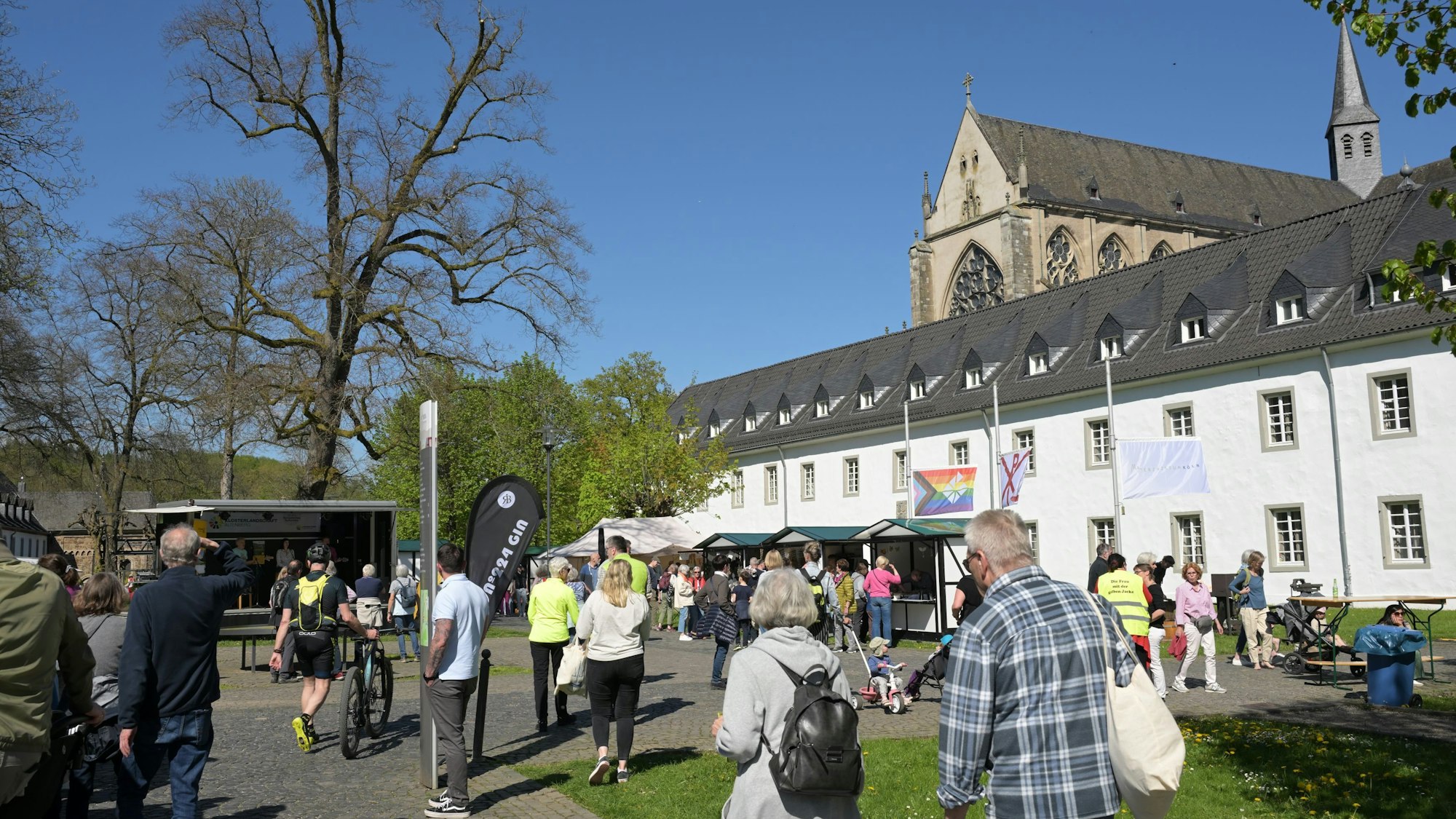 Der Altenberger Dom, davor das gebäude der Jugendbildungsstätte haus Altenberg und viele Menschen an Ständen an einem sommerlichen Tag.