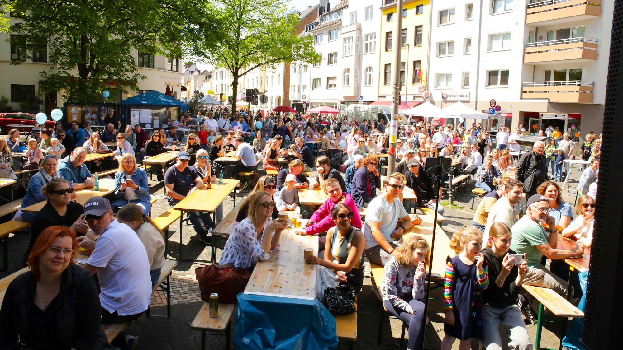 Menschen sitzen bei „Bunt Im Carrée“ auf Bänken und gucken einem Auftritt auf der Bühne zu.