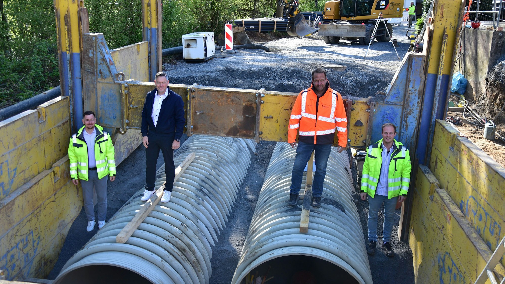 In der Baustelle für den neuen Stauraumkanal in Much stehen Michael Hoppe (Gemeindewerke Much), Bürgermeister Karsten Schäfer, Bauleiter Kai Vogel und Kanalsanierungsberater Johannes Urbach auf den großen Röhren.