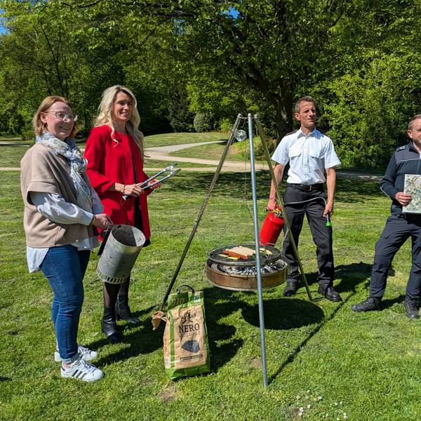 Zwei Frauen und zwei Männer stehen um einen Grill auf einer Wiese.