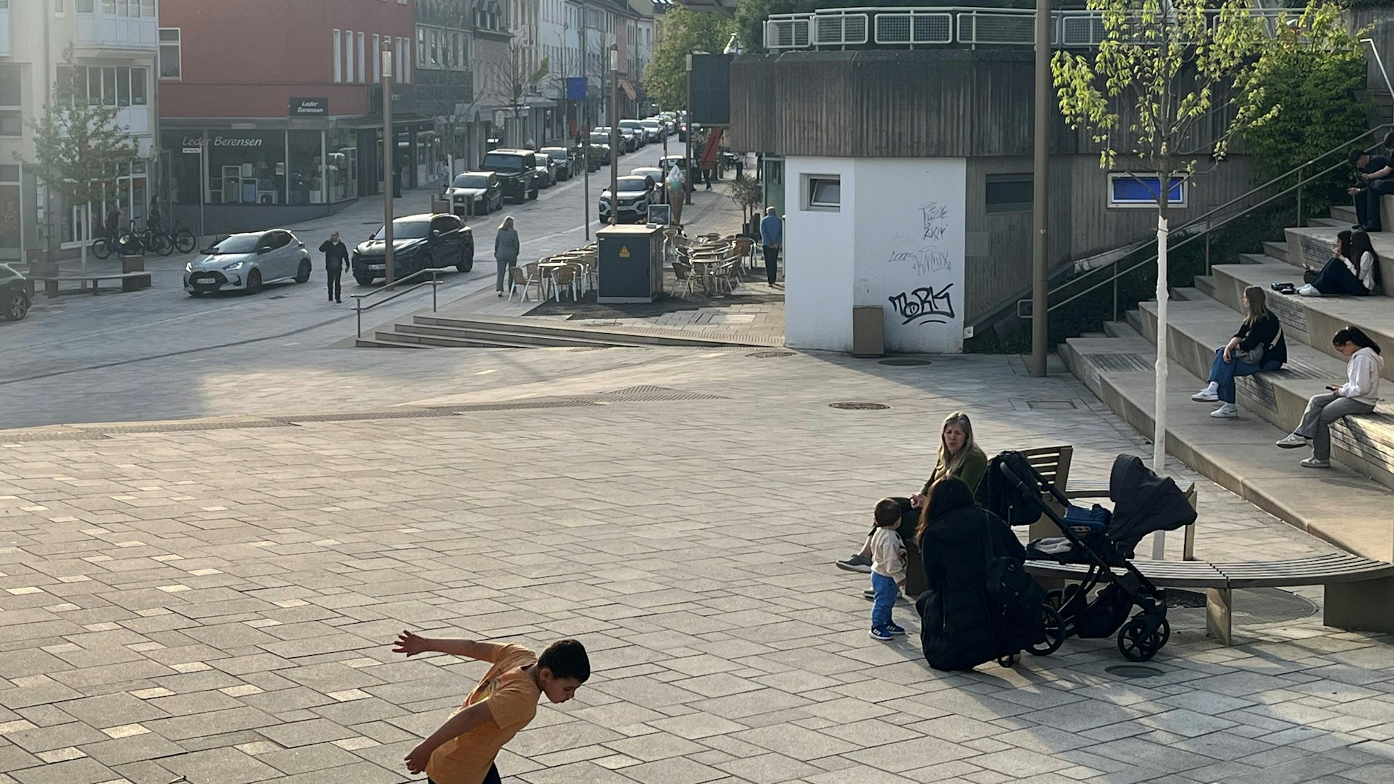 Menschen sitzen auf einer Bank, ein Junge spielt Fußball.