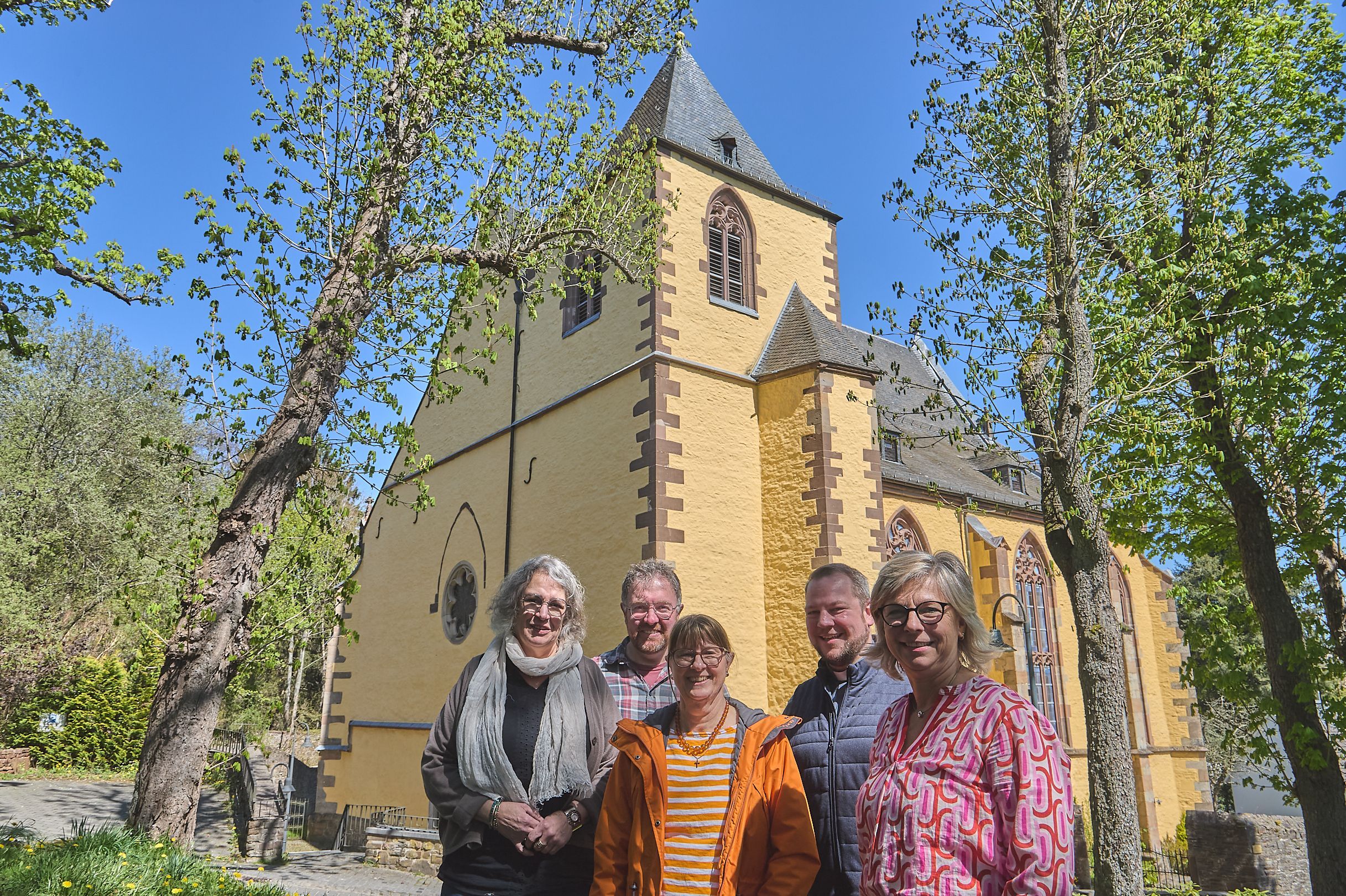 Das neue Leitungsteam des Pastoralen Raumes Hellenthal/Schleiden steht vor einer Kirche.