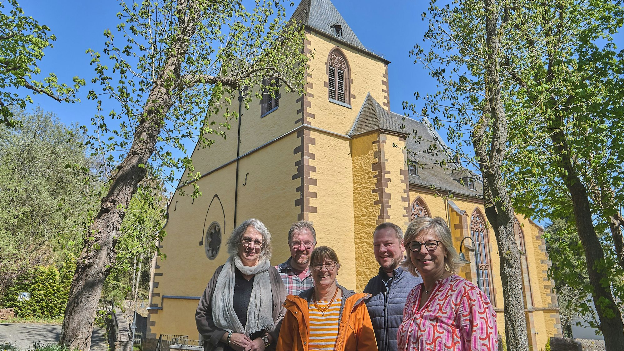 Das neue Leitungsteam des Pastoralen Raumes Hellenthal/Schleiden steht vor einer Kirche.