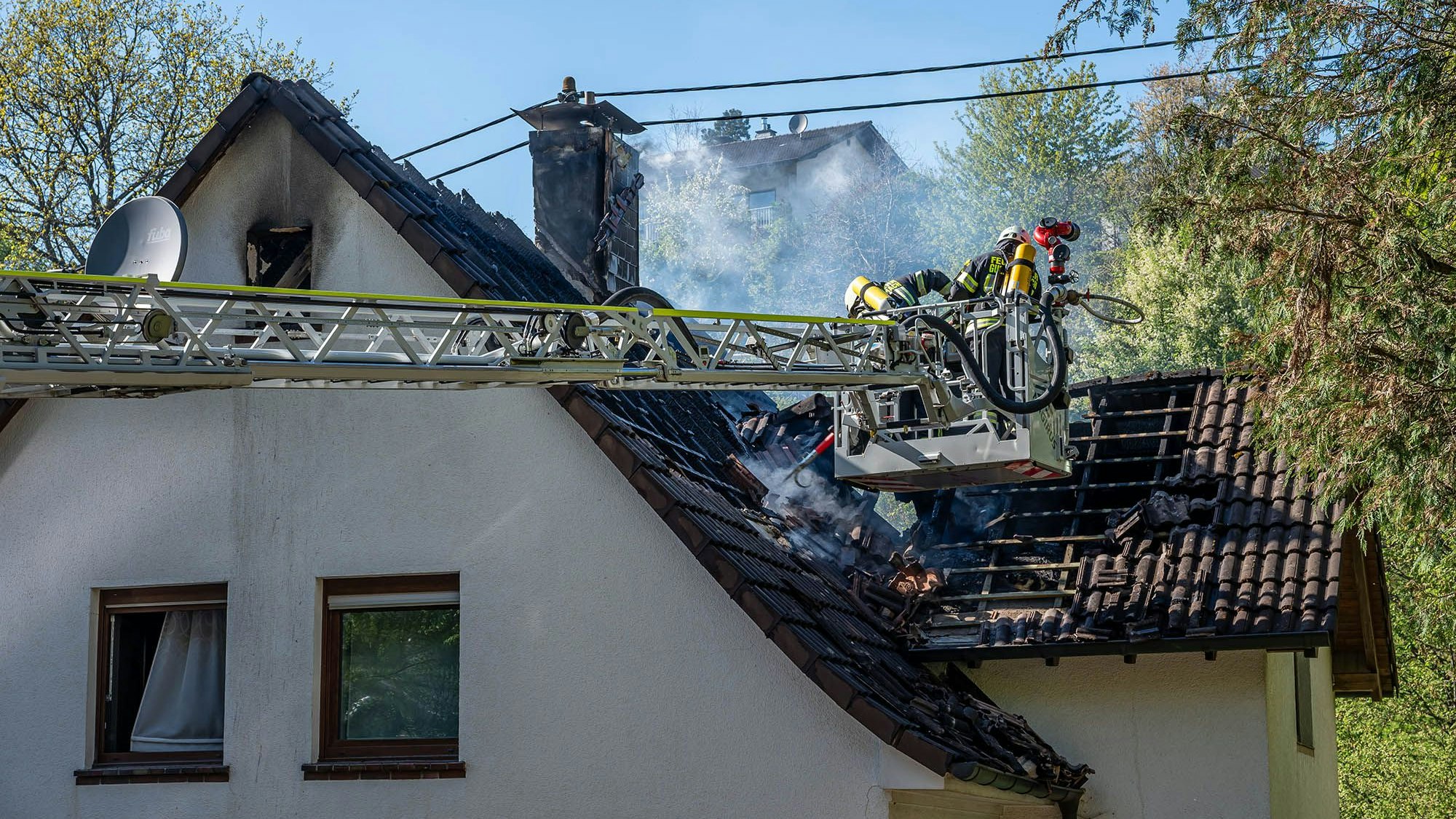 Feuerwehrleute löschen von einer Drehleiter aus einen Dachstuhlbrand.