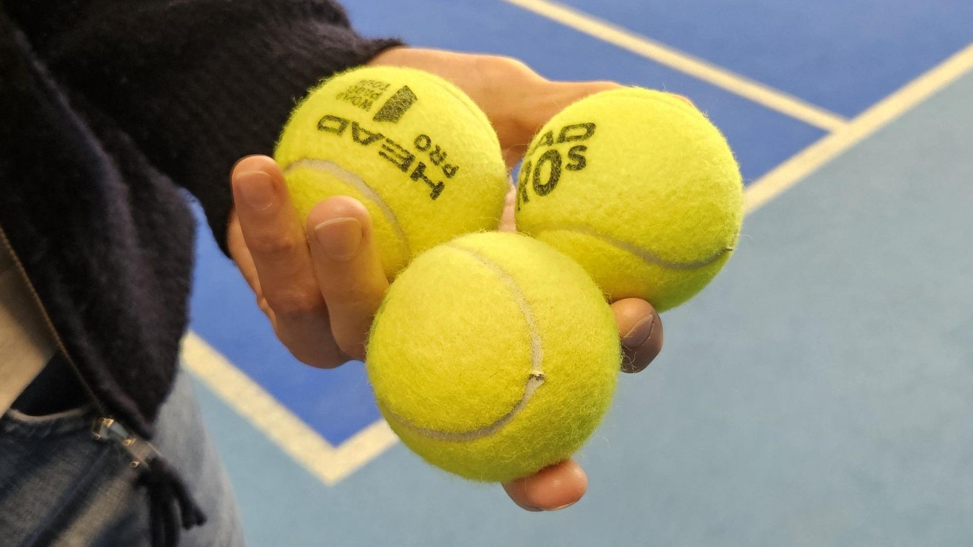 Jemand hält drei Padel-Bälle in der Hand.