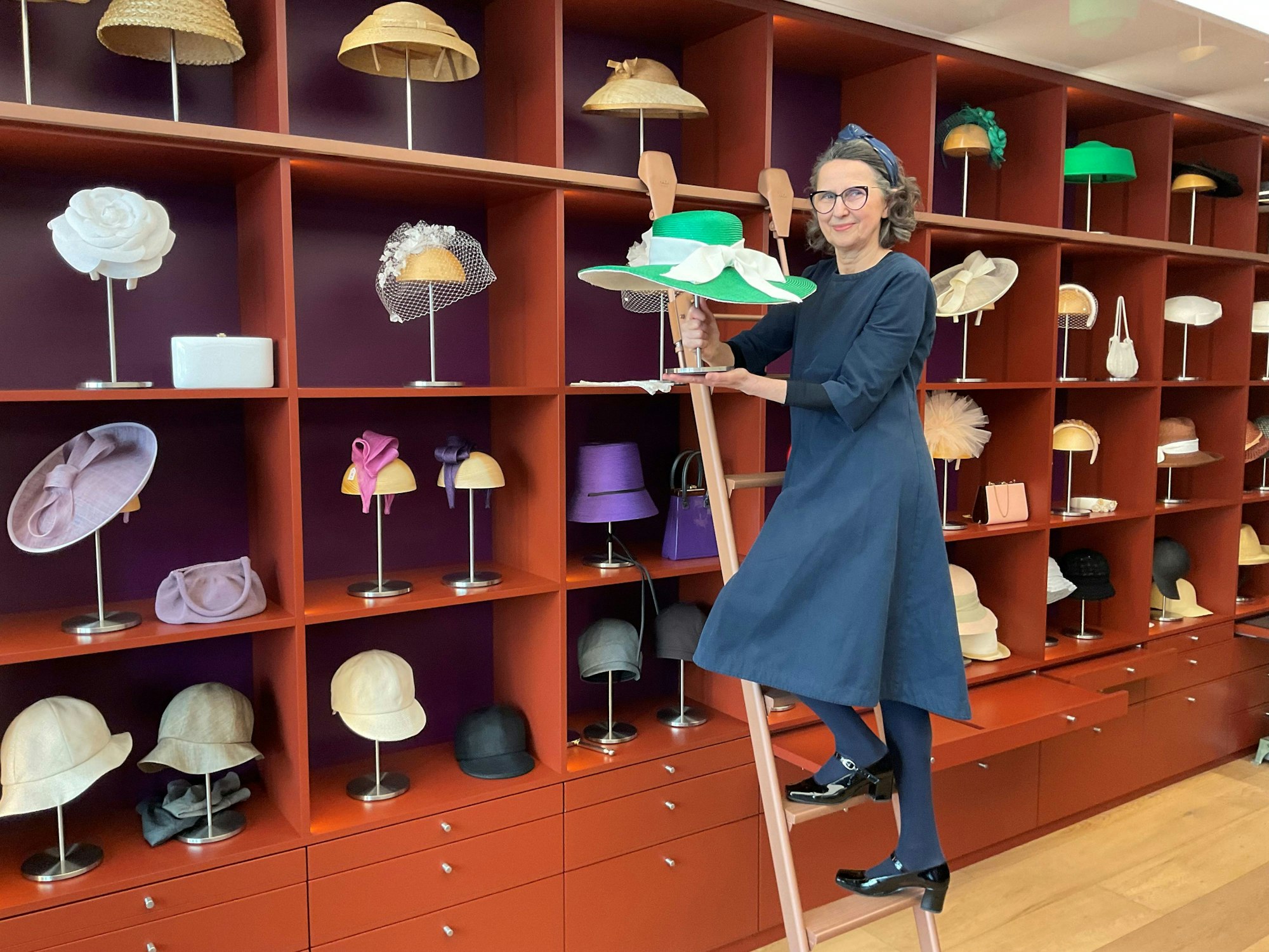 Eine Frau steht auf einer Leiter, die vor einem großen Regal mit Hüten steht.