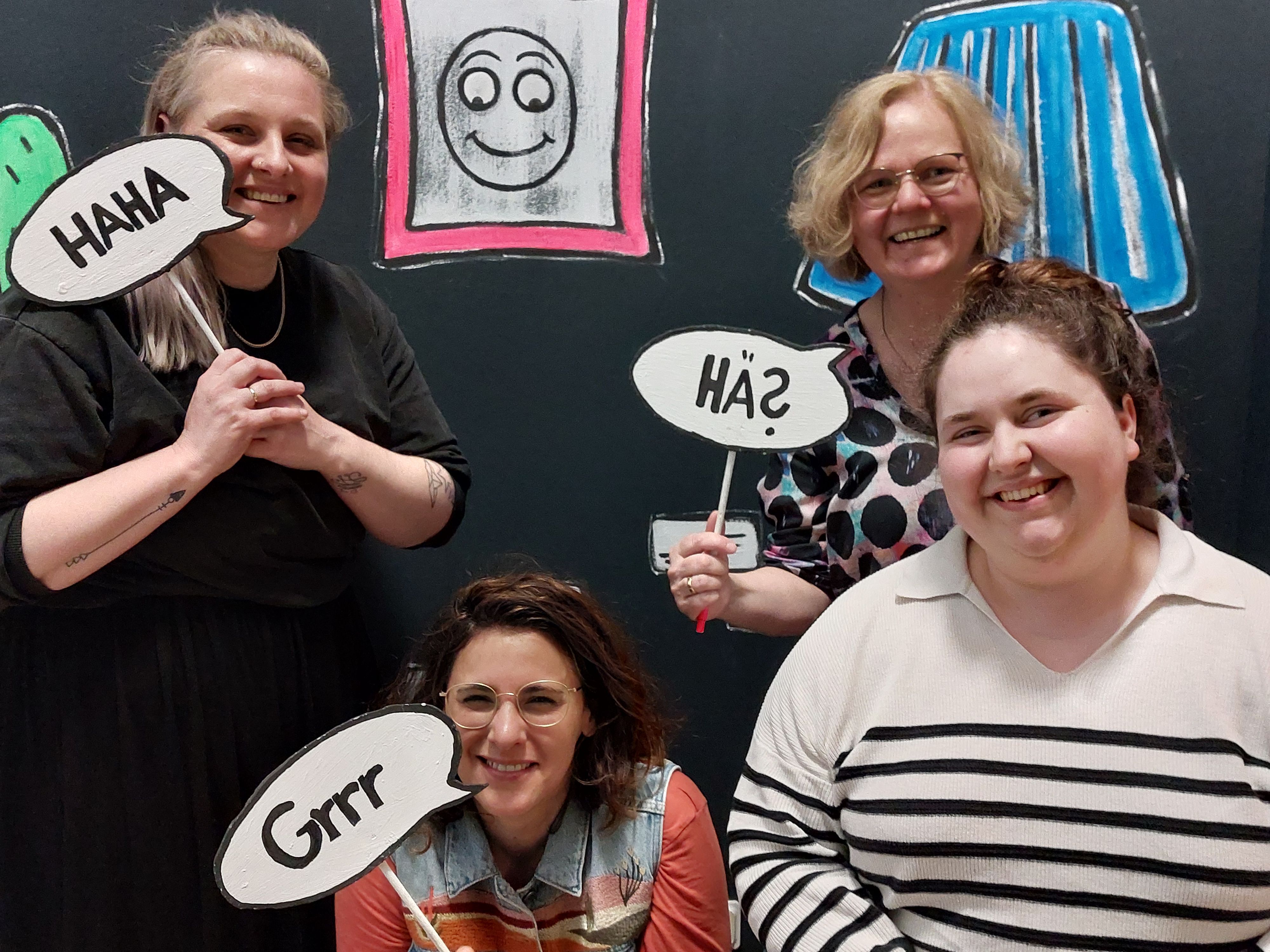 Vier Frauen halten Comicsprechblasen an Holzstäben.