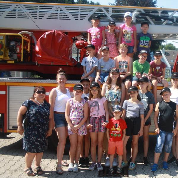 Eine Gruppe von Kindern und Betreuerinnen steht um und auf einem Drehleiterfahrzeug der Feuerwehr.