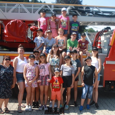 Eine Gruppe von Kindern und Betreuerinnen steht um und auf einem Drehleiterfahrzeug der Feuerwehr.