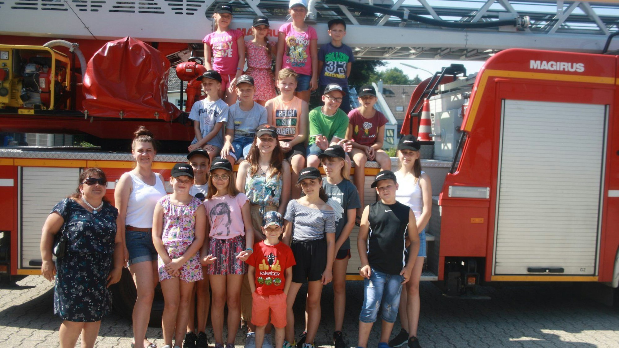 Eine Gruppe von Kindern und Betreuerinnen steht um und auf einem Drehleiterfahrzeug der Feuerwehr.