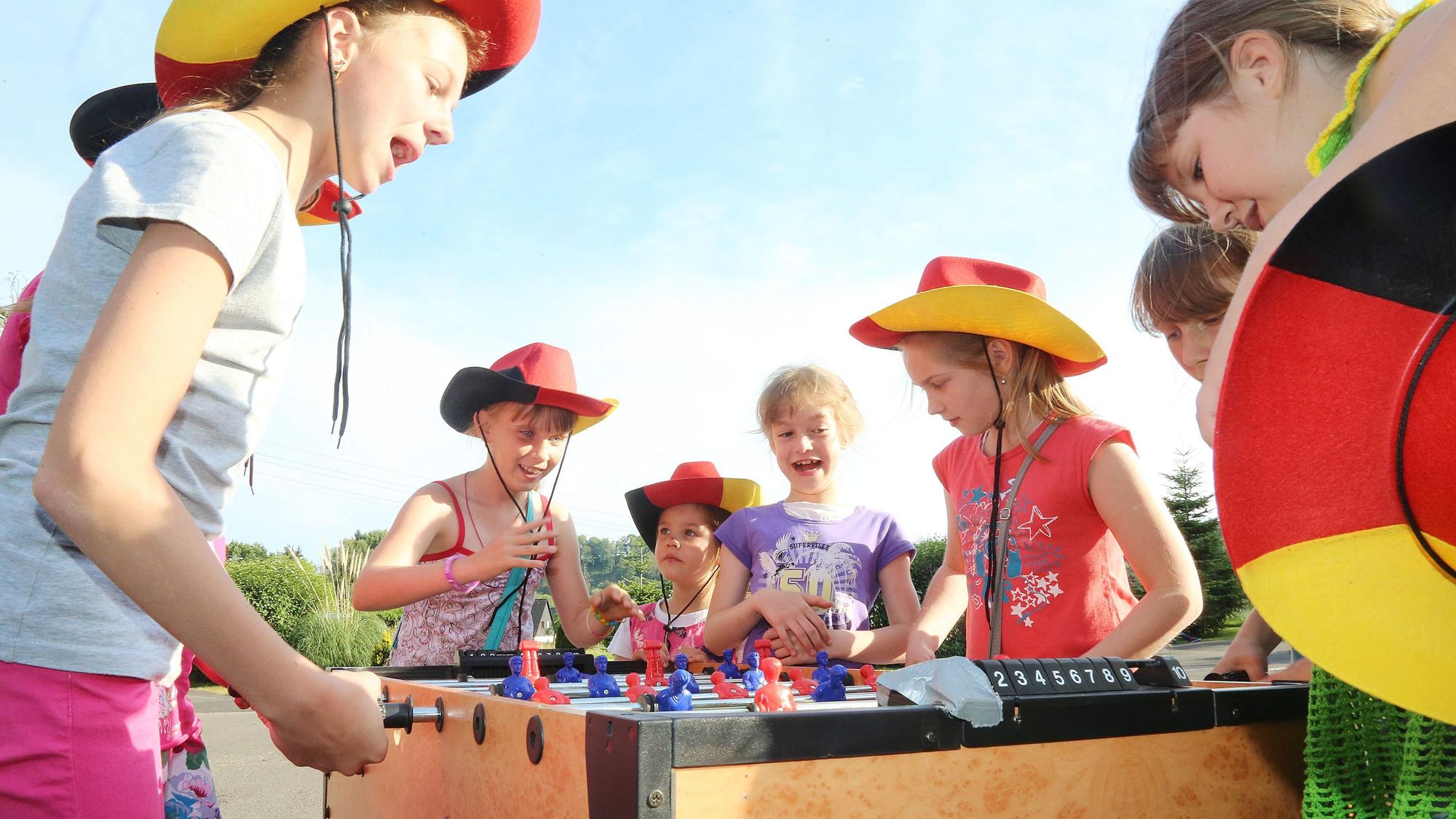 Kinder mit Hüten in Schwarz-Rot-Gold spielen an einem Tischkicker.