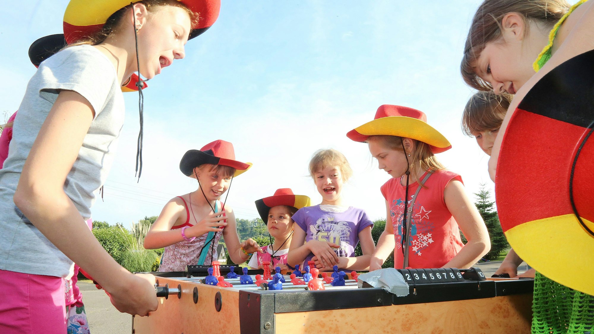 Kinder mit Hüten in Schwarz-Rot-Gold spielen an einem Tischkicker.