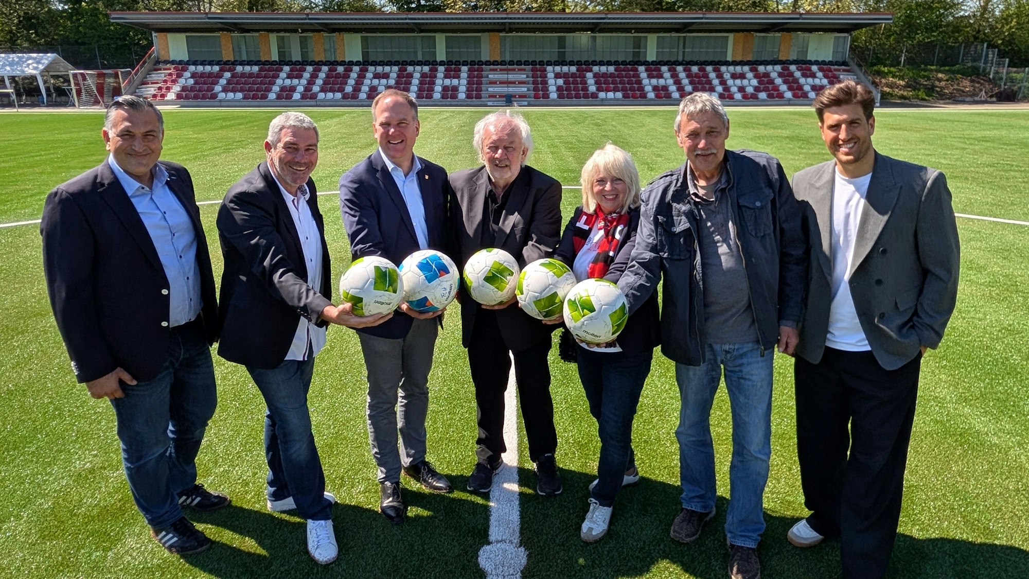 Das Foto zeigt Vertreterinnen und Vertreter der Stadt und des FC Hürth auf dem Kunstrasen vor der Tribüne im Salus-Park.