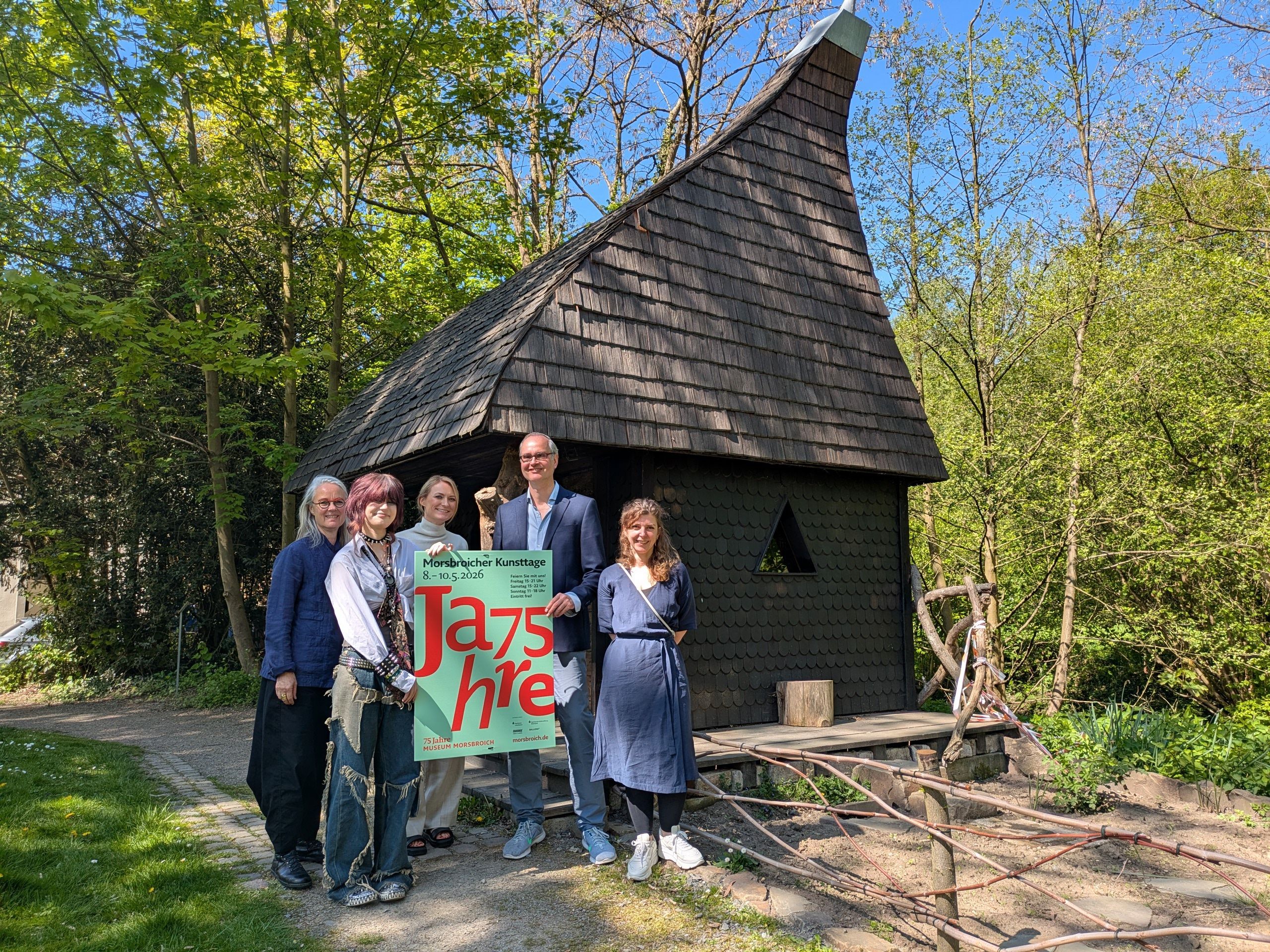 Ein Mann und vier Frauen stehen vor dem Witches Cottage im Park von Schloss Morsbroich