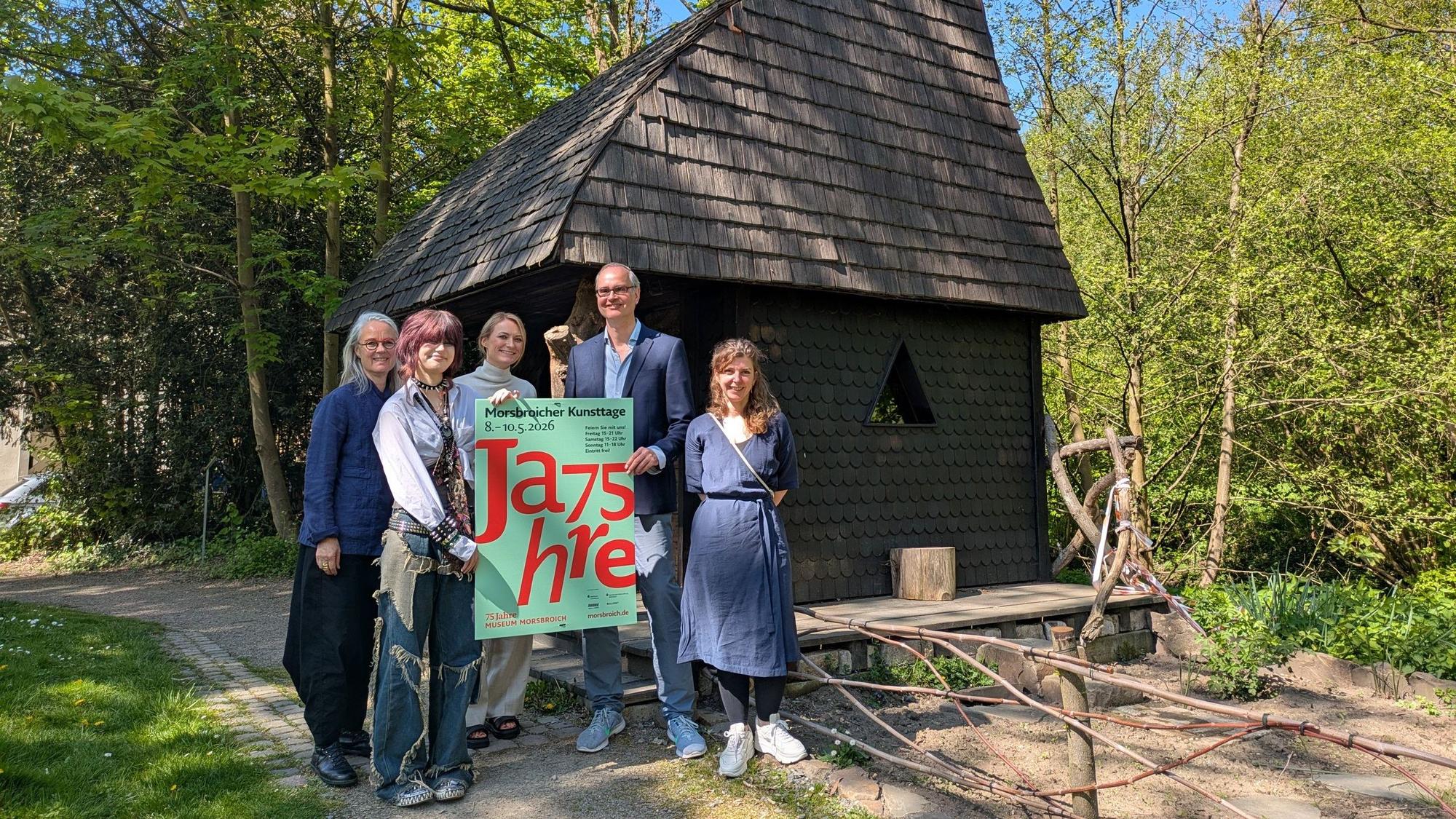 Ein Mann und vier Frauen stehen vor dem Witches Cottage im Park von Schloss Morsbroich