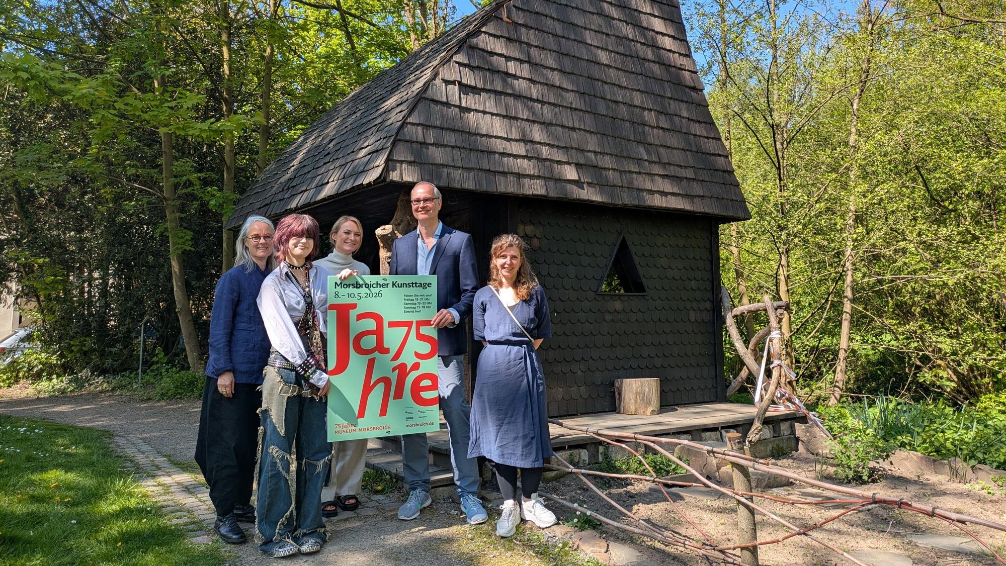 Ein Mann und vier Frauen stehen vor dem Witches Cottage im Park von Schloss Morsbroich