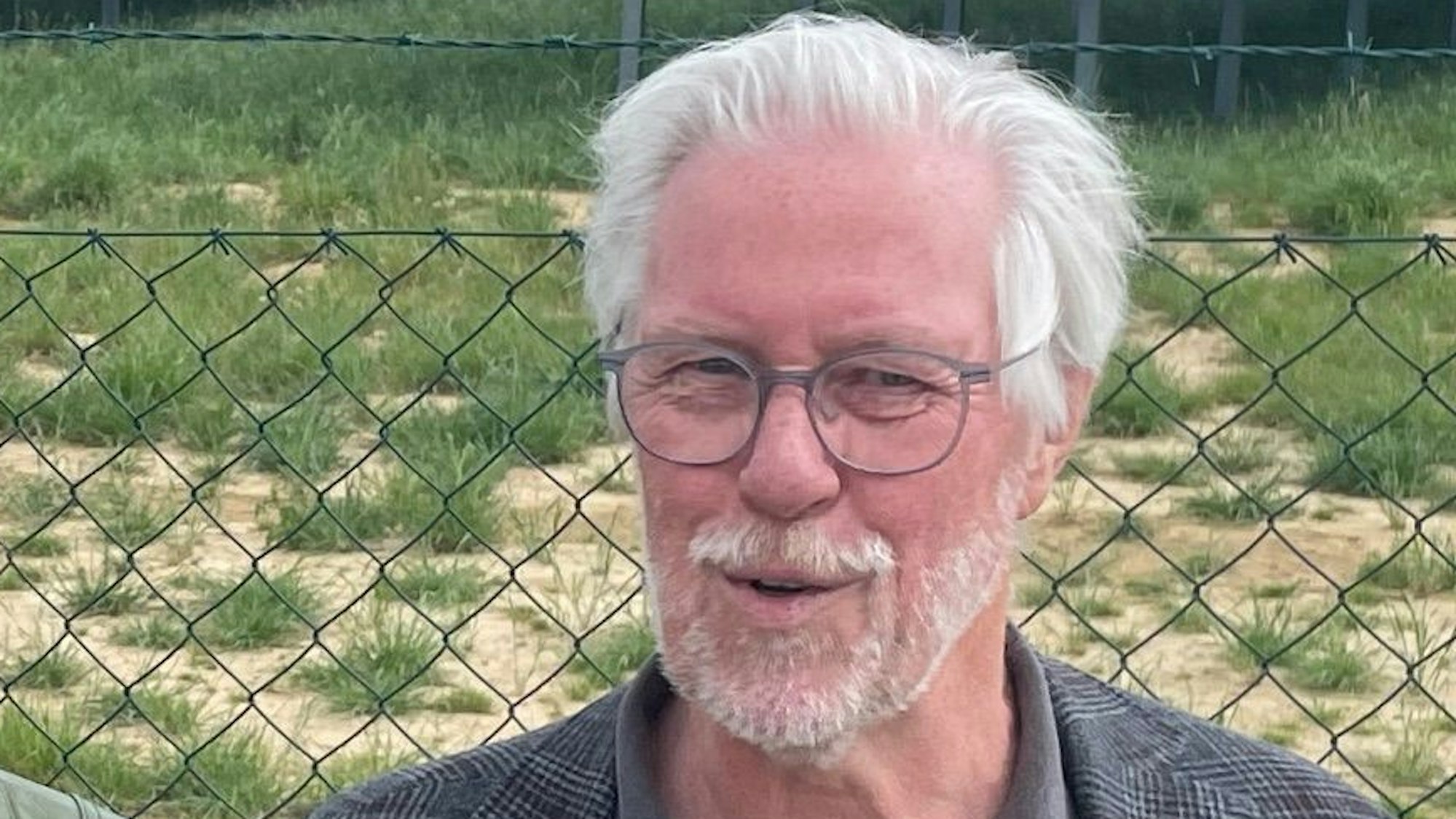 Auf dem Foto ist ein Mann mit Brille, grauem Haar und grauem Bart zu sehen.