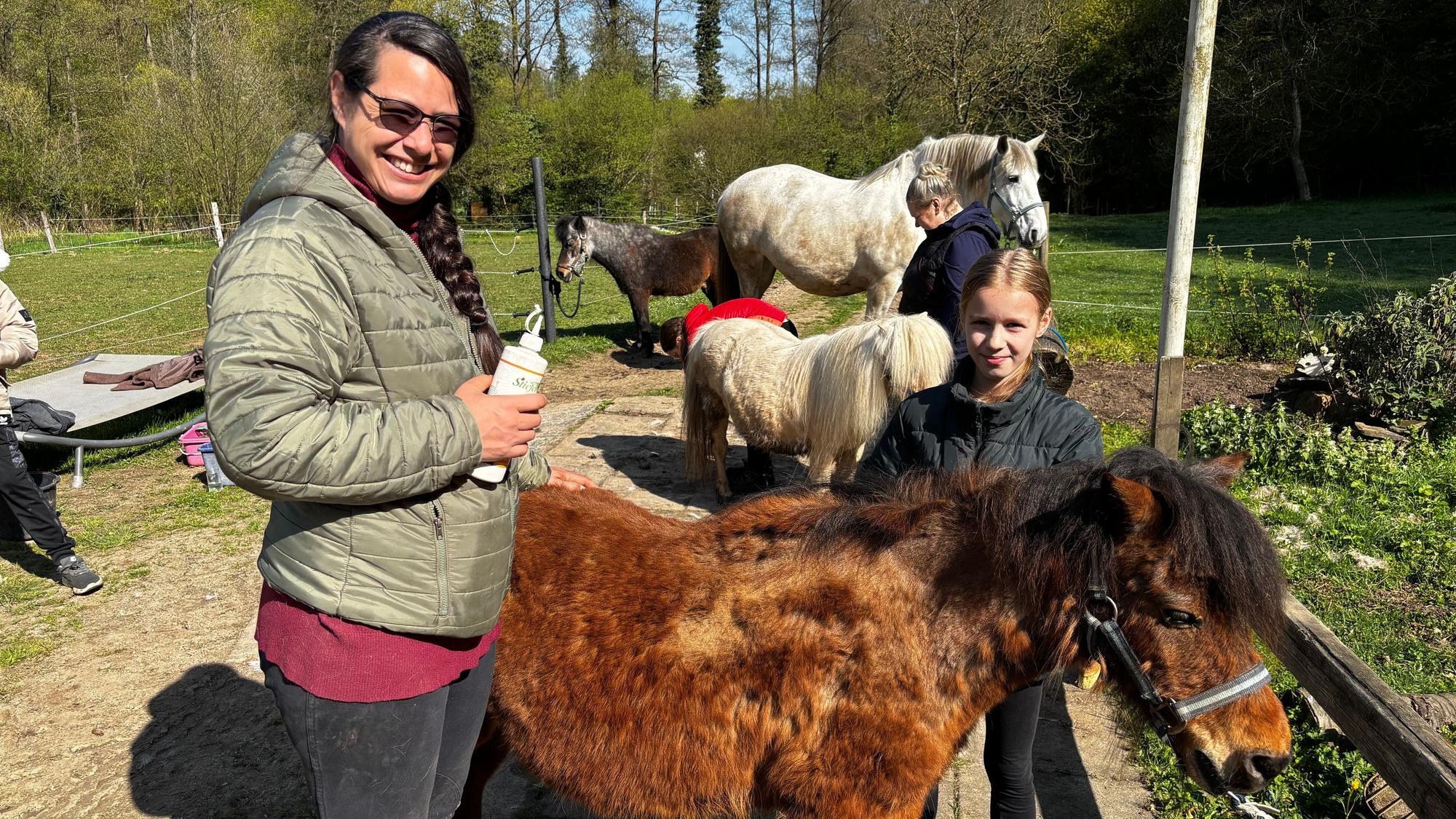 Eine Frau und ein Mädchen blicken lächelnd in die Kamera. Ein braunes Shetlandpony steht zwischen ihnen.