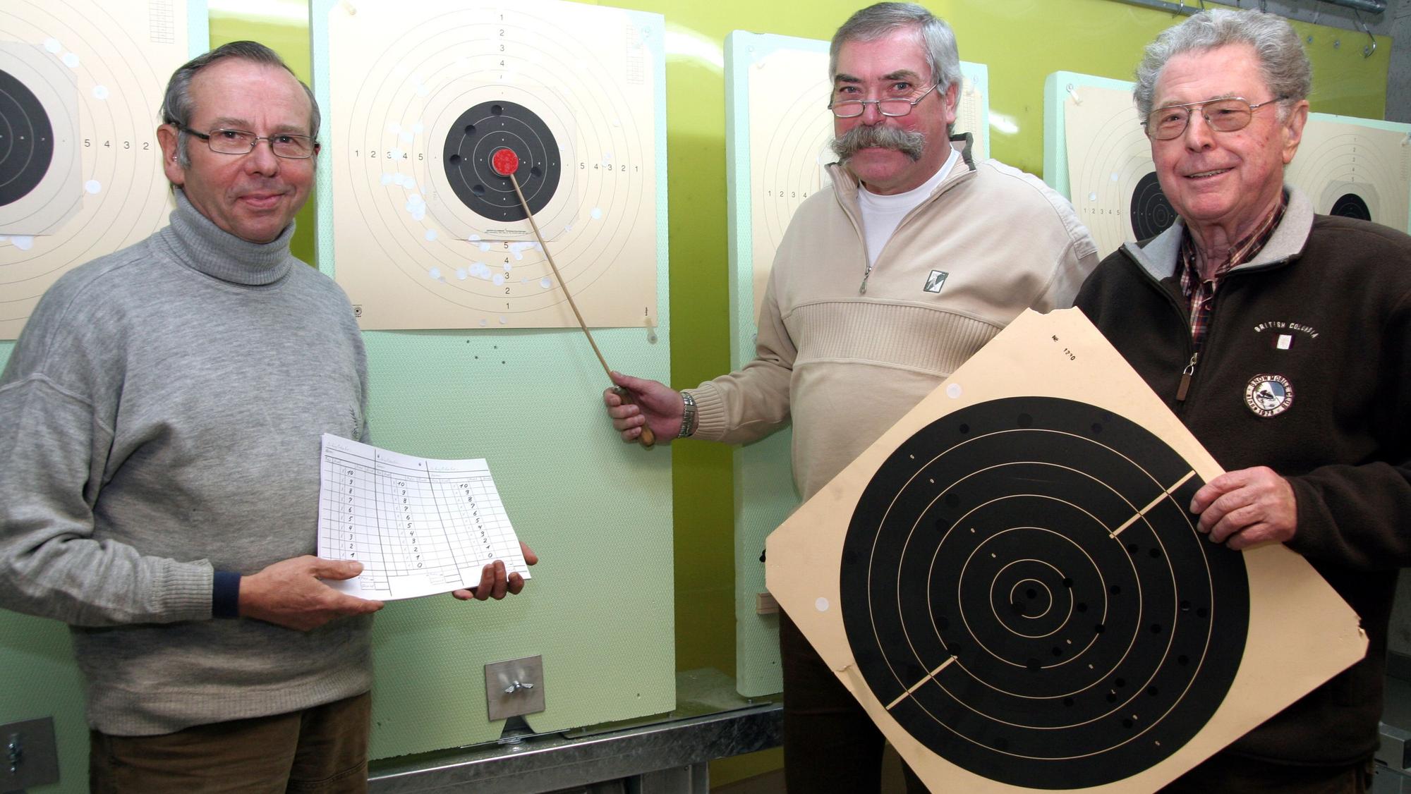 Drei Sportschützen stehen an einer Zielscheibe.