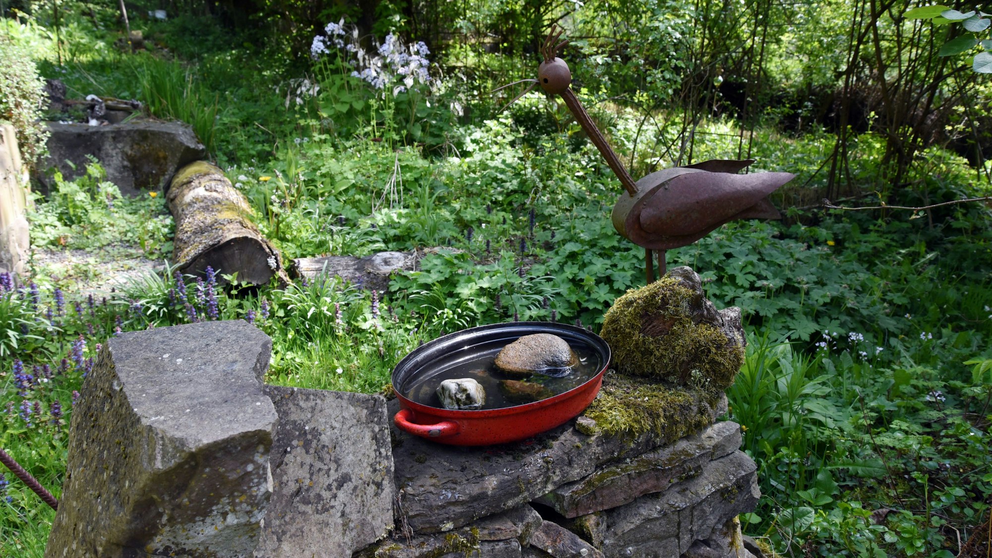 Ein Metallvogel auf einer Gartenmauer.