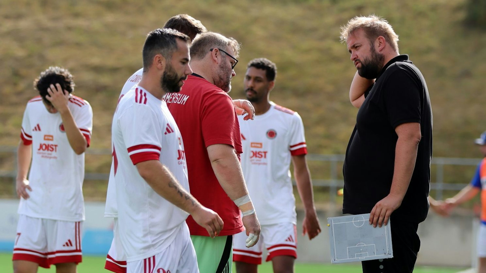 Sebastian Reisenauer steht am Spielfeldrand, In der Hand hält er eine kleine Taktiktafel.