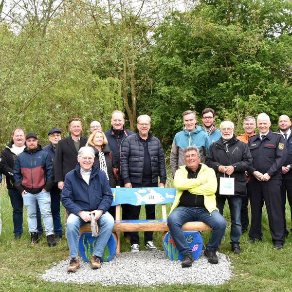 Zwei Männer sitzen auf einer Bank, hinter stehen Frauen und Männer.