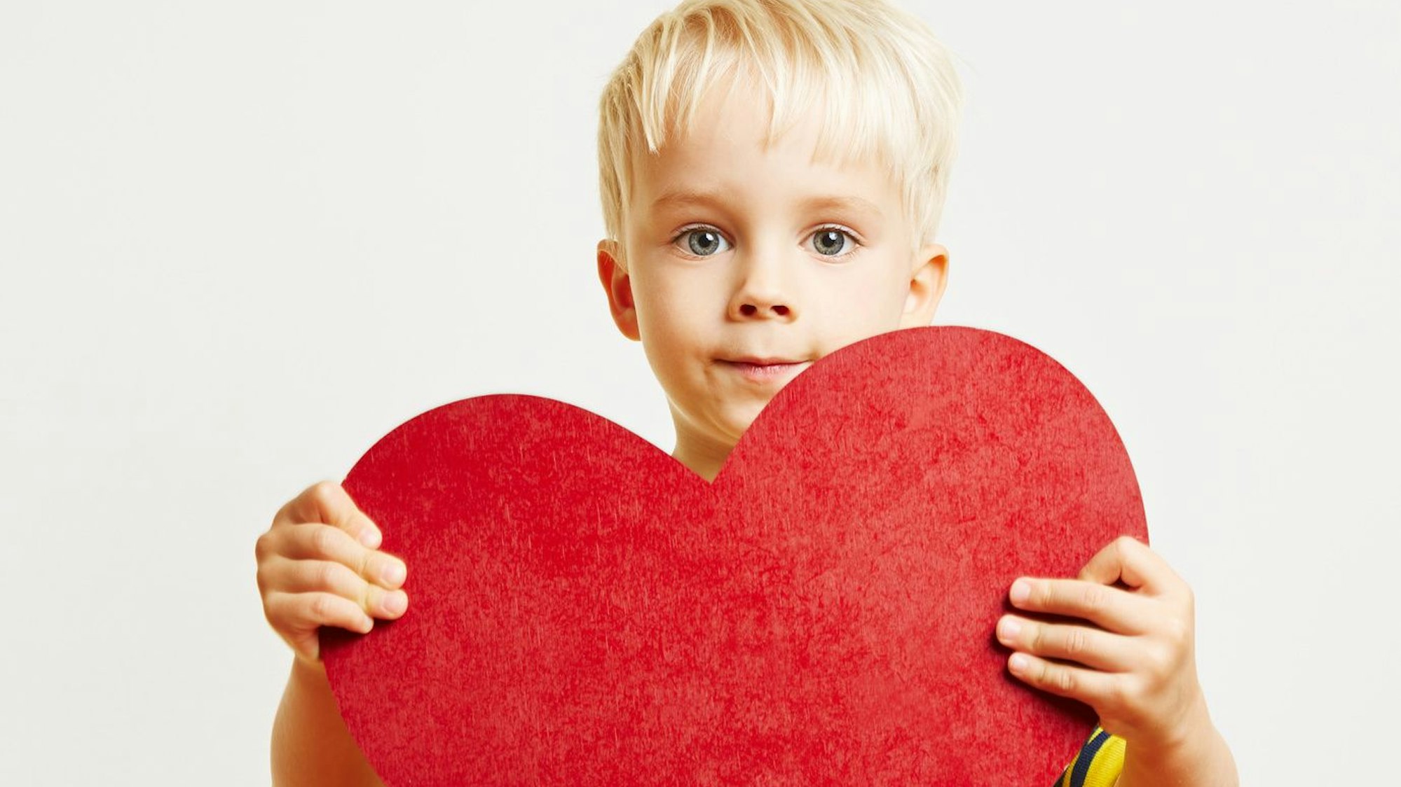 Ein blonder Junge hält ein großes rotes Herz in den Händen