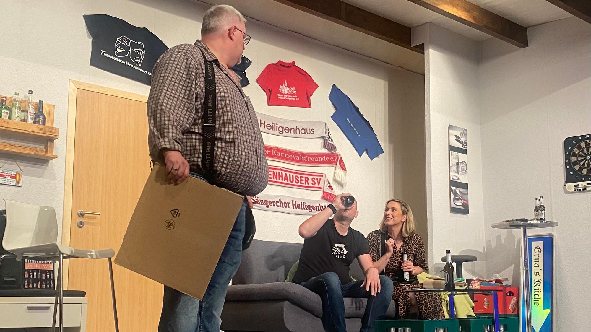 Auf einem Sofa sitzen zwei Personen, daneben steht ein Mann im Karohemd.