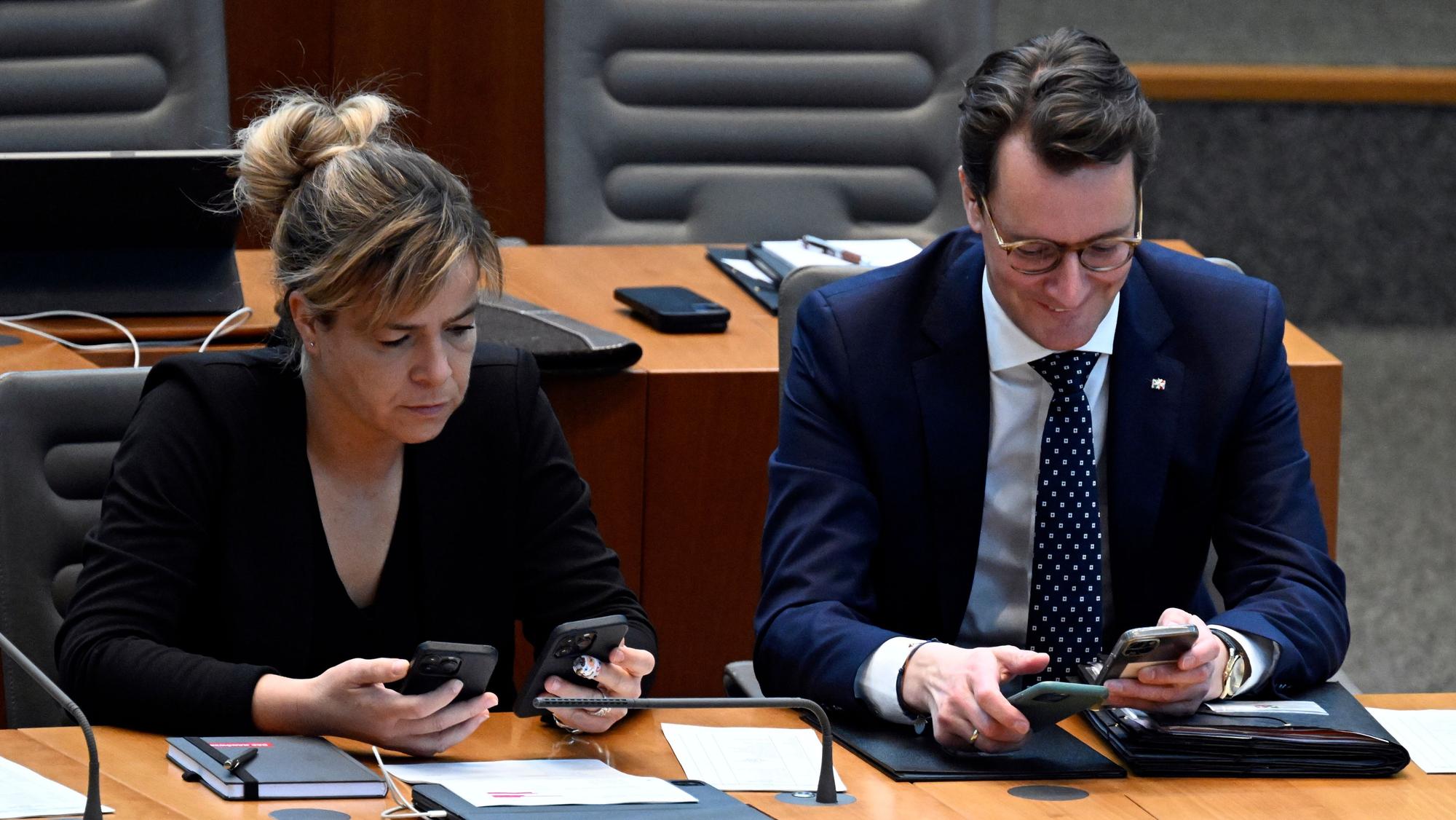 Hendrik Wüst (CDU, r.), Ministerpräsident von Nordrhein-Westfalen, und Mona Neubaur (Bündnis 90/Die Grünen), Ministerin für Wirtschaft, Industrie, Klimaschutz und Energie von Nordrhein-Westfalen, schauen im Landtag vor Beginn des bundesweiten Probealarms am Warntag auf ihre Handys.