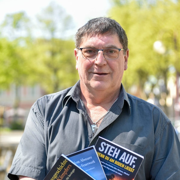 Das Foto zeigt das Portrait eines Mannes mit Brille und einem grauen Hemd.