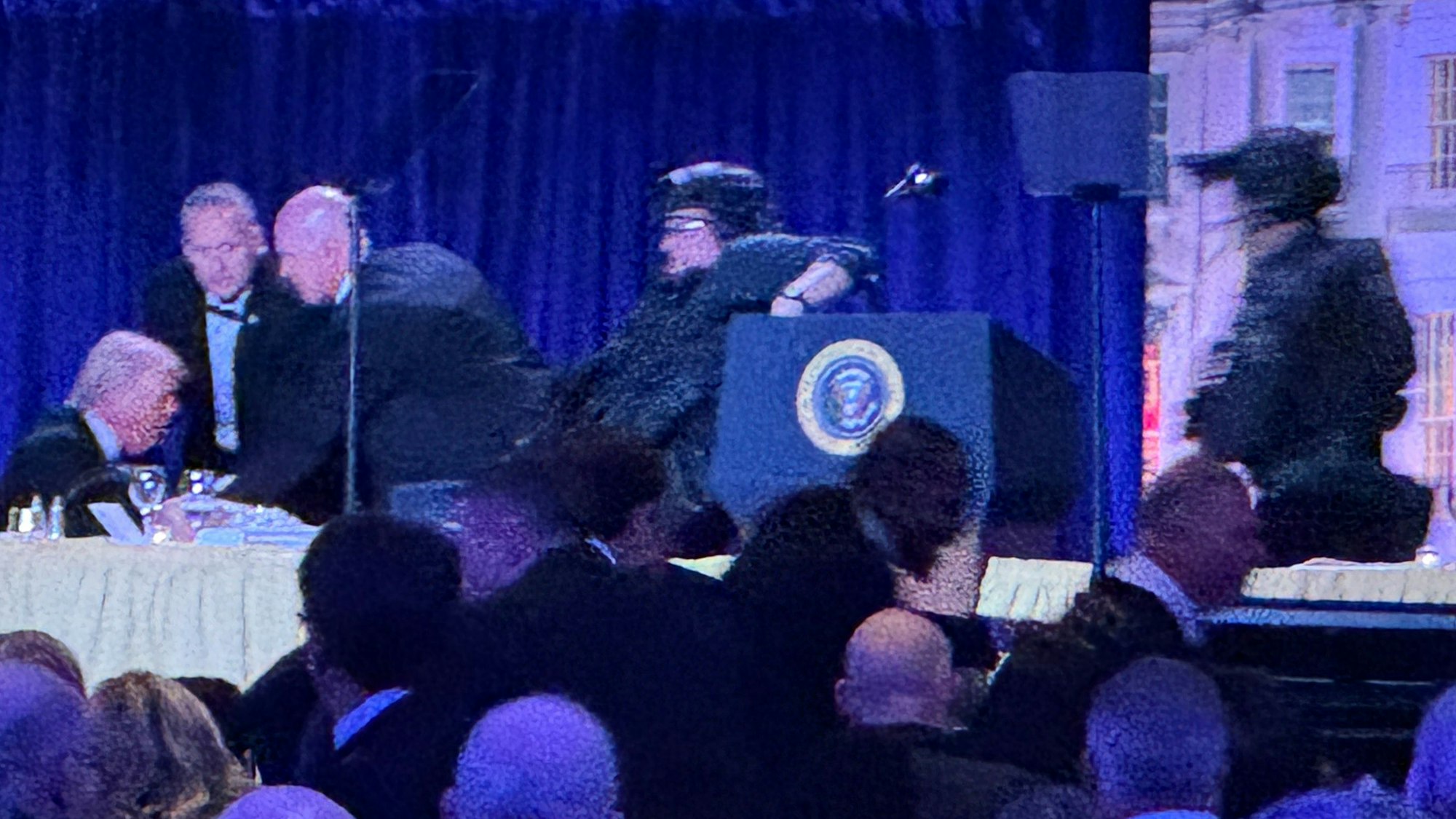 US-Präsident Donald Trump (l) sitzt auf der Bühne, während Agenten des US-Geheimdienstes ihn nach einem Vorfall außerhalb des Ballsaals während des White House Correspondents' Dinner aus dem Ballsaal bringen.
